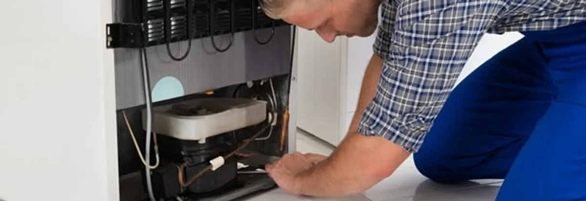 Refrigerator repair technician servicing the compressor and condenser area in West Palm Beach, FL