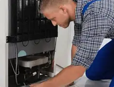 Refrigerator repair technician servicing the compressor and condenser area in West Palm Beach, FL